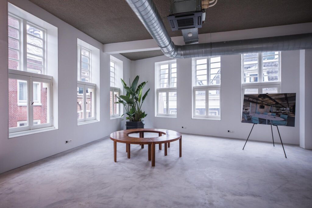 Licht en modern interieur aan de Prins Hendrikkade met ronde houten tafel, grote plant en presentatiescherm.